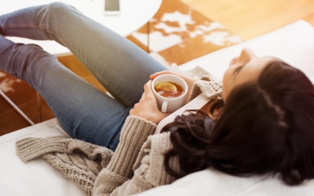 Frau entspannt mit einer Tasse Tee auf dem Sofa