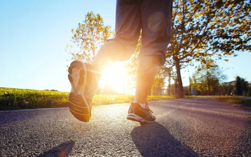 Beine eines Läufers auf einer Asphaltstraße im Gegenlicht der Sonne