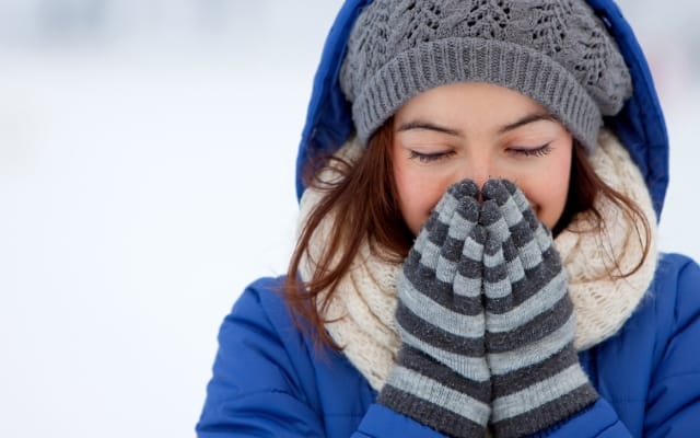 Frau in Winterkleidung mit Mütze und Handschuhen wärmt sich die Hände im Schnee