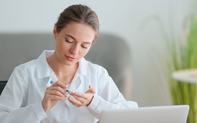 Frau misst ihren Blutzucker mit einer Stechhilfe am Finger