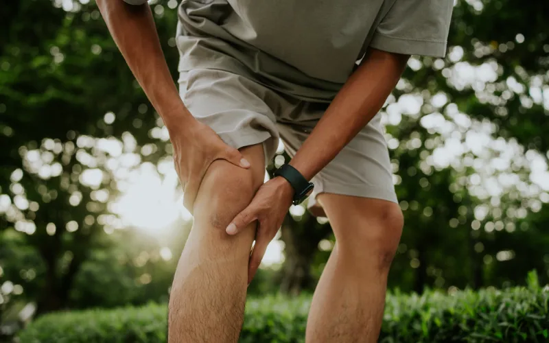 Mann hält sich im Freien mit beiden Händen das Knie