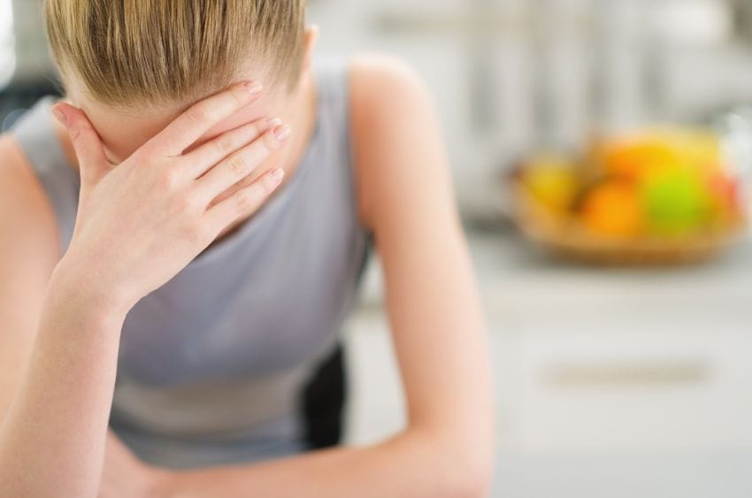 Erschöpfte Frau stützt den Kopf in der Küche in die Hand