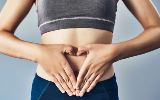 Frau formt mit den Händen ein Herz auf ihrem Bauch