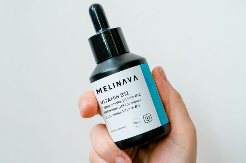 Hand hält eine Pipettenflasche MELINAVA Vitamin B12