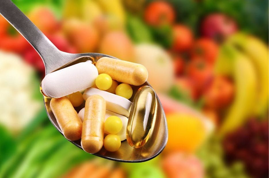 Löffel mit Kapseln und Tabletten vor Obst und Gemüse