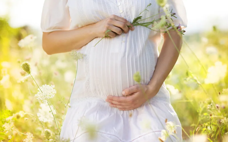 Schwangere Frau in weißem Kleid auf einer Blumenwiese