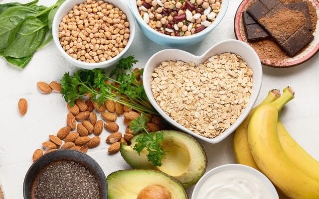 Schalen mit Hülsenfrüchten, Haferflocken, Mandeln, Chiasamen, Avocado, Bananen und Zartbitterschokolade